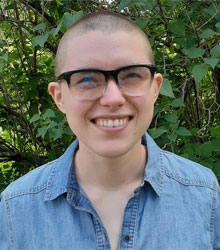 Gabrielle Martin headshot in a blue shirt, dark rimmed glasses, shaved head, smiling 