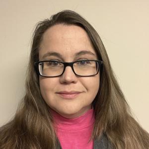 Melissa Birch - white woman slightly smiling with shoulder-length light brown hair, wearing dark rectangle-framed glasses, a pink turtleneck shirt and a black cardigan